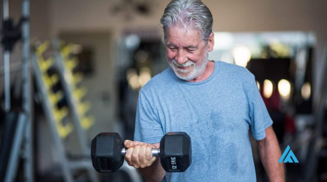 A senior man engaged in strength training for adults over 50, confidently holding a dumbbell in a gym, exemplifying fitness and perseverance.
