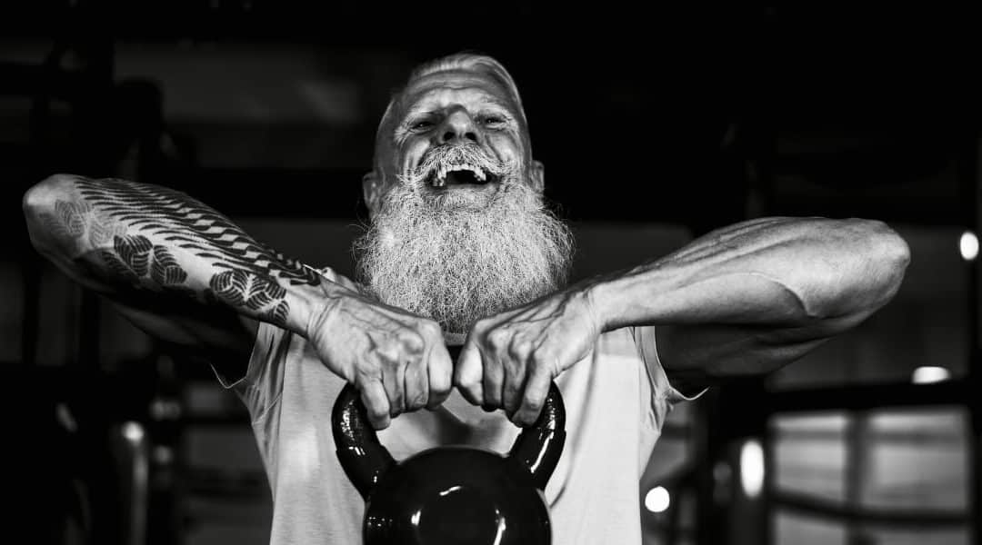 Older adult with a beard lifting a kettlebell in a gym, showcasing strength and resilience through strength and conditioning training for adults over 50.